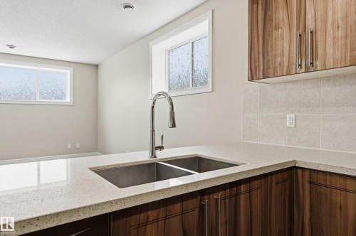 Kitchen featuring light stone countertops, decorative backsplash, and a textured ceiling - 1346 Cunningham Drive W, Edmonton, AB - Indoor Photo Showing Kitchen With Double Sink