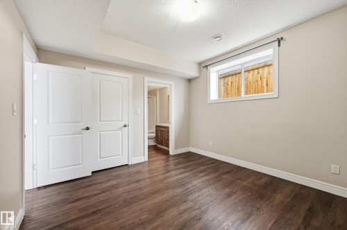 Unfurnished bedroom with connected bathroom, dark wood-style flooring, and a textured ceiling - 1346 Cunningham Drive W, Edmonton, AB - Indoor Photo Showing Other Room