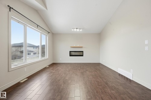 Unfurnished living room featuring a glass covered fireplace, dark wood-style floors, and vaulted ceiling - 1346 Cunningham Drive W, Edmonton, AB - Indoor With Fireplace
