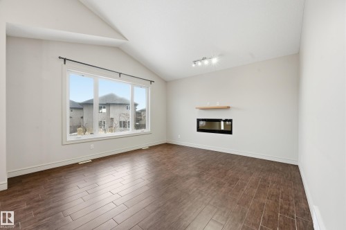 Unfurnished living room with wood finish floors, a glass covered fireplace, and lofted ceiling - 1346 Cunningham Drive W, Edmonton, AB - Indoor Photo Showing Living Room With Fireplace