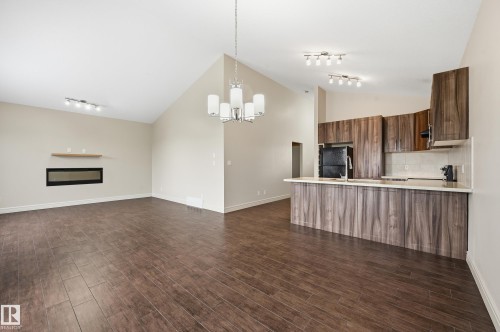 Unfurnished living room with dark wood-type flooring, a glass covered fireplace, hanging lights, and vaulted ceiling - 1346 Cunningham Drive W, Edmonton, AB - Indoor Photo Showing Kitchen