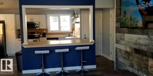 Kitchen with light countertops, a peninsula, stainless steel appliances, white cabinets, and a kitchen bar - 13524 62 Street, Edmonton, AB - Indoor Photo Showing Kitchen