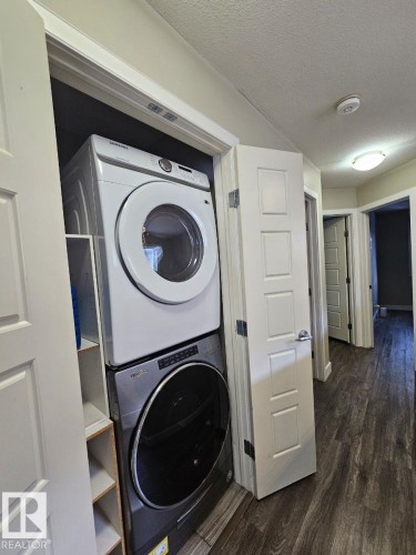 Laundry area featuring dark wood-type flooring, stacked washer and clothes dryer, and a textured ceiling - 208 Kirpatrick Way, Leduc, AB - Indoor Photo Showing Laundry Room
