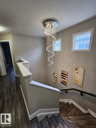 Staircase featuring a chandelier, wood finished floors, and a textured ceiling - 208 Kirpatrick Way, Leduc, AB - Indoor Photo Showing Other Room
