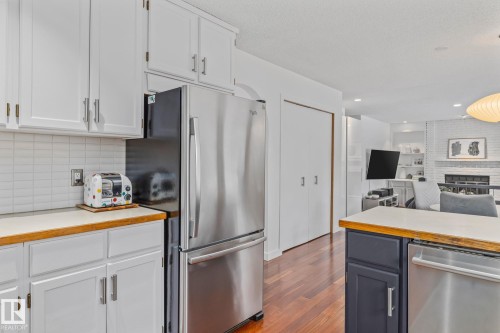 Kitchen featuring stainless steel appliances, dark wood-type flooring, open floor plan, white cabinetry, and a brick fireplace - 175 Roy Street, Edmonton, AB - Indoor Photo Showing Kitchen