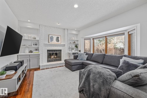 Living area featuring dark wood-style floors, a textured ceiling, a brick fireplace, recessed lighting, and built in shelves - 175 Roy Street, Edmonton, AB - Indoor Photo Showing Living Room With Fireplace
