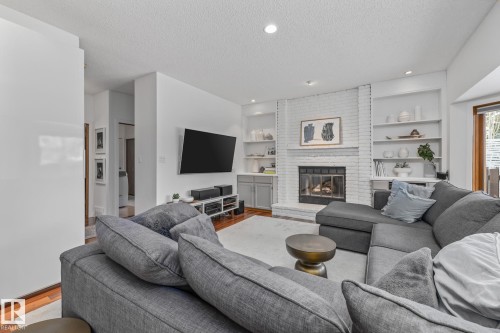 Living room featuring wood finished floors, a textured ceiling, a brick fireplace, recessed lighting, and built in shelves - 175 Roy Street, Edmonton, AB - Indoor Photo Showing Living Room With Fireplace