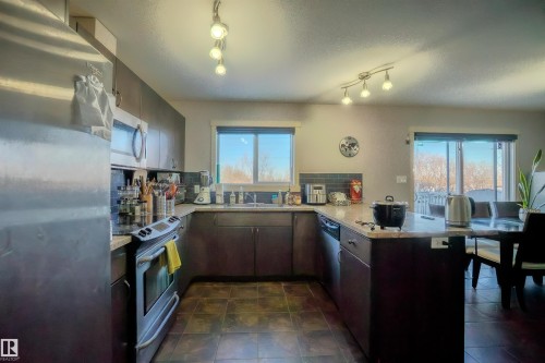 Kitchen featuring stainless steel appliances, backsplash, a peninsula, a textured ceiling, and dark wood finish cabinets - 5244 1A Avenue Sw, Edmonton, AB - Indoor Photo Showing Kitchen