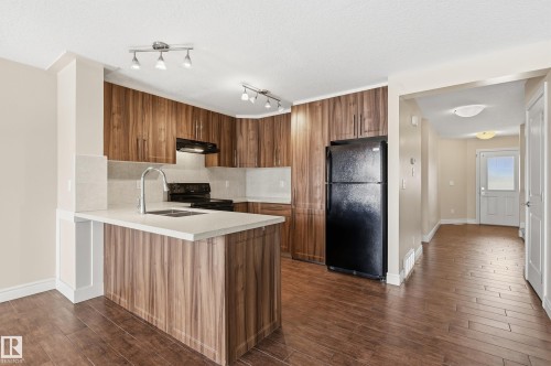 Kitchen featuring wood finish cabinets, black appliances, dark wood-style floors, a peninsula, and a textured ceiling - 1349 Cunningham Drive, Edmonton, AB - Indoor Photo Showing Kitchen