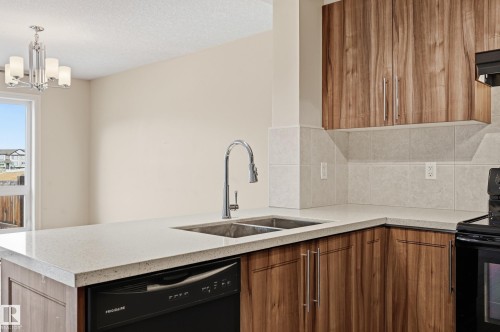 Kitchen featuring black appliances, wood finish cabinetry, tasteful backsplash, light stone countertops, and a chandelier - 1349 Cunningham Drive, Edmonton, AB - Indoor Photo Showing Kitchen With Double Sink