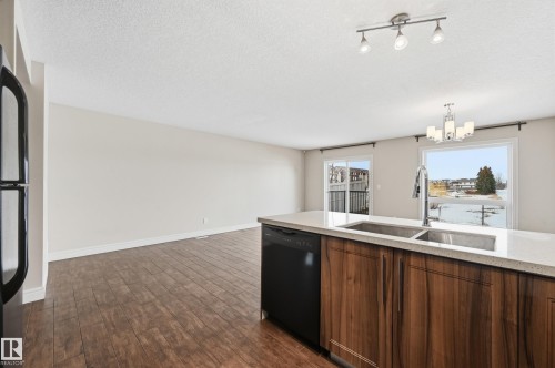 Kitchen featuring dishwasher, light stone countertops, dark wood-type flooring, suspended lighting, and stainless steel refrigerator - 1349 Cunningham Drive, Edmonton, AB - Indoor Photo Showing Kitchen With Double Sink