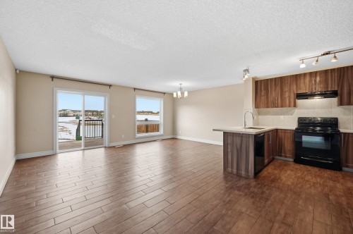 Kitchen with black appliances, a peninsula, open floor plan, dark wood finished floors, and a textured ceiling - 1349 Cunningham Drive, Edmonton, AB - Indoor