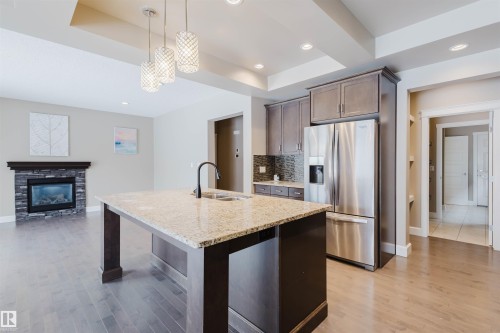 Kitchen with stainless steel fridge with ice dispenser, open floor plan, light stone counters, a raised ceiling, and a kitchen island with sink - 1957 Ainslie Link, Edmonton, AB - Indoor Photo Showing Kitchen With Stainless Steel Kitchen With Double Sink With Upgraded Kitchen
