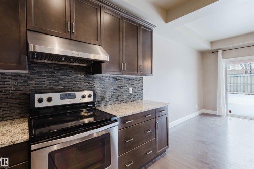 Kitchen with electric stove, dark wood finish cabinets, and light stone countertops - 1957 Ainslie Link, Edmonton, AB - Indoor Photo Showing Kitchen