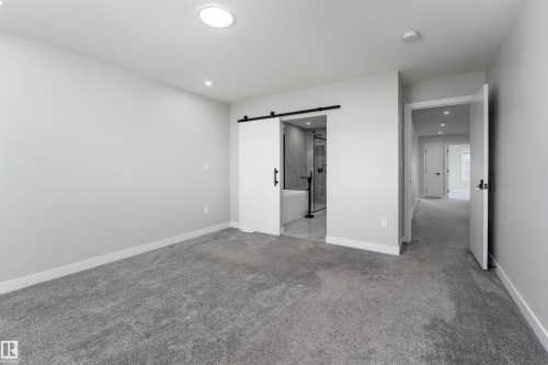 Unfurnished bedroom featuring light carpet, a barn door, a textured ceiling, recessed lighting, and ensuite bathroom - 5211 Kimball Crescent, Edmonton, AB - Indoor Photo Showing Other Room