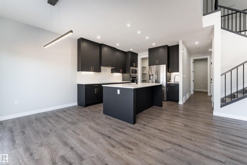 Kitchen with a center island with sink, dark cabinetry, open floor plan, dark wood-type flooring, and stainless steel appliances - 5211 Kimball Crescent, Edmonton, AB - Indoor Photo Showing Kitchen With Upgraded Kitchen