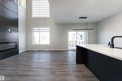 Unfurnished living room featuring dark wood-style floors, plenty of natural light, a high ceiling, and a large fireplace - 5211 Kimball Crescent, Edmonton, AB - Indoor With Fireplace
