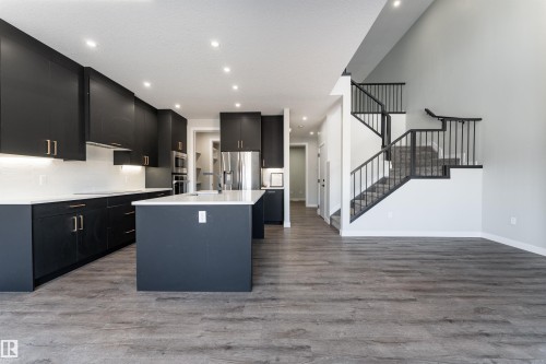 Kitchen featuring dark cabinets, an island with sink, light wood finished floors, stainless steel appliances, and recessed lighting - 5211 Kimball Crescent, Edmonton, AB - Indoor Photo Showing Kitchen With Upgraded Kitchen