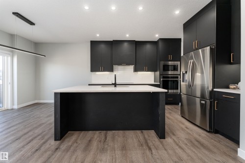 Kitchen featuring dark cabinets, stainless steel appliances, a kitchen island with sink, light wood-type flooring, and tasteful backsplash - 5211 Kimball Crescent, Edmonton, AB - Indoor Photo Showing Kitchen With Upgraded Kitchen
