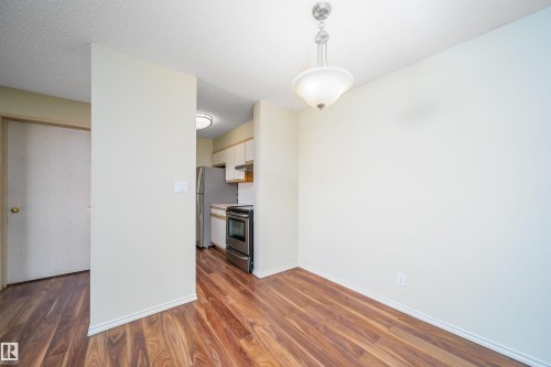 Kitchen featuring hanging light fixtures, dark wood-type flooring, a textured ceiling, stainless steel appliances, and light countertops - 213 5065 31 Avenue, Edmonton, AB - Indoor