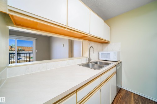 Kitchen with white microwave, light countertops, dark wood-style floors, stainless steel dishwasher, and two tone color scheme - 213 5065 31 Avenue, Edmonton, AB - Indoor Photo Showing Kitchen With Double Sink