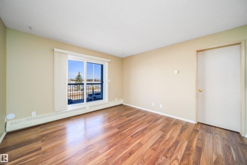 Empty room featuring a baseboard heating unit, dark wood-style flooring, and a textured ceiling - 213 5065 31 Avenue, Edmonton, AB - Indoor Photo Showing Other Room