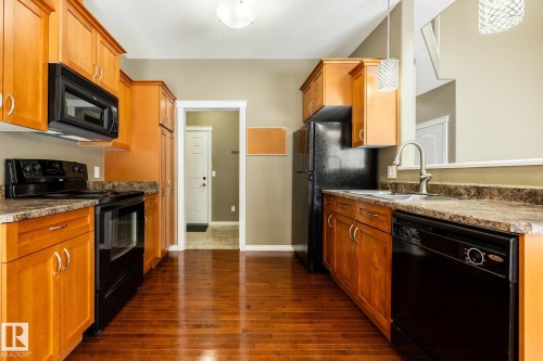 Kitchen with black appliances, wood finish cabinets, dark wood-style flooring, and dark countertops - 11622 11 Avenue, Edmonton, AB - Indoor Photo Showing Kitchen With Double Sink