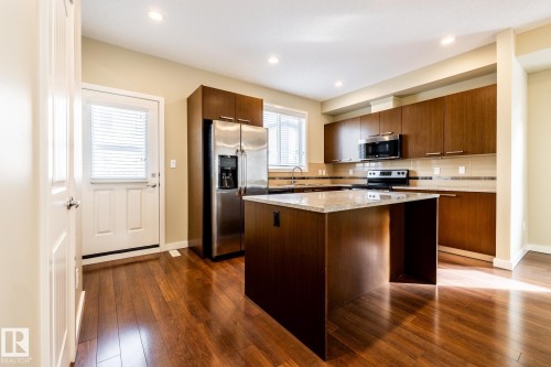 Kitchen featuring stainless steel appliances, dark wood-type flooring, a center island, light stone countertops, and decorative backsplash - 21 655 Watt Boulevard, Edmonton, AB - Indoor Photo Showing Kitchen