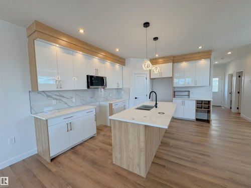 Two tone kitchen with an island with sink, decorative backsplash, two tone cabinets, light wood finished floors, and modern cabinets - 7 Tilia Place, Spruce Grove, AB - Indoor Photo Showing Kitchen With Double Sink With Upgraded Kitchen