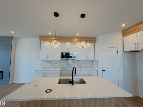 Kitchen featuring light wood finished floors, decorative light fixtures, white cabinets, light stone counters, and an island with sink - 7 Tilia Place, Spruce Grove, AB - Indoor Photo Showing Kitchen
