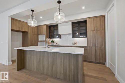 Kitchen featuring modern cabinets, pendant lighting, brown cabinets, light wood-style floors, and glass insert cabinets - 6704 Crawford Way, Edmonton, AB - Indoor Photo Showing Kitchen With Upgraded Kitchen