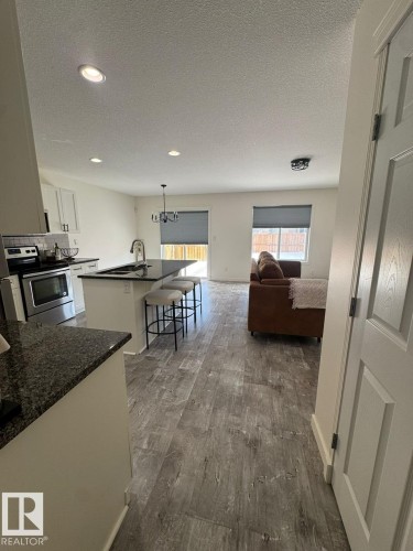 Kitchen with a kitchen bar, an island with sink, electric stove, white cabinetry, and a textured ceiling - 17703 65 Street, Edmonton, AB - Indoor Photo Showing Other Room