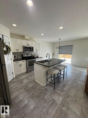 Kitchen with stainless steel appliances, a textured ceiling, white cabinets, an island with sink, and a kitchen breakfast bar - 17703 65 Street, Edmonton, AB - Indoor Photo Showing Kitchen