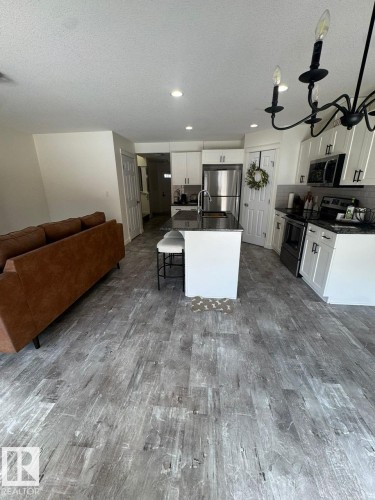 Kitchen with open floor plan, stainless steel appliances, an island with sink, a breakfast bar area, and dark stone counters - 17703 65 Street, Edmonton, AB - Indoor