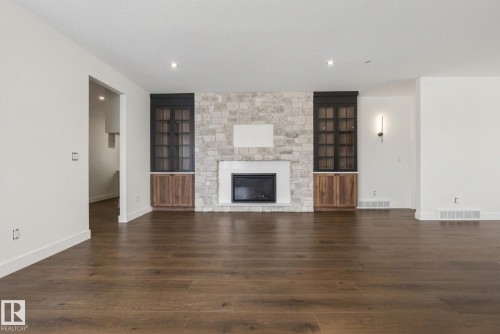 Unfurnished living room featuring dark wood-style flooring, a stone fireplace, built in features, a textured ceiling, and recessed lighting - 149 Eastgate Way, St. Albert, AB - Indoor Photo Showing Living Room With Fireplace