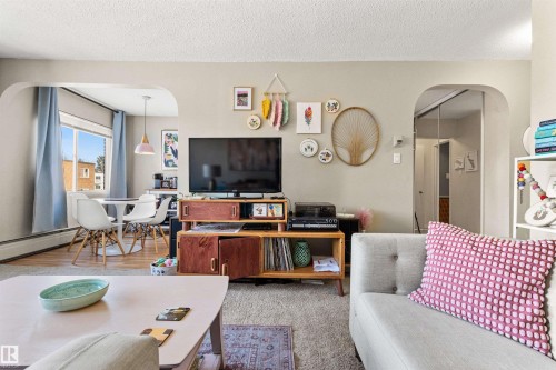 Living room featuring arched walkways, a textured ceiling, and a baseboard heating unit - 304 11420 40 Avenue Nw, Edmonton, AB - Indoor Photo Showing Living Room