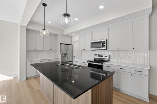 Kitchen featuring stainless steel appliances, a kitchen island with sink, dark stone counters, light wood-style floors, and decorative light fixtures - 22 Grayson Green, Stony Plain, AB - Indoor Photo Showing Kitchen With Double Sink With Upgraded Kitchen