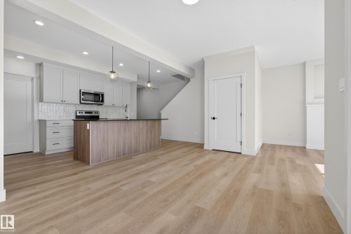 Two tone kitchen with an island with sink, two tone cabinets, light wood-style flooring, decorative light fixtures, and backsplash - 22 Grayson Green, Stony Plain, AB - Indoor Photo Showing Kitchen