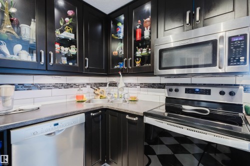 Kitchen with stainless steel appliances, dark cabinets, glass fronted cabinets, backsplash, and light countertops - 1803 10149 Saskatchewan Drive, Edmonton, AB - Indoor Photo Showing Kitchen