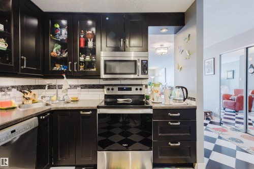 Kitchen featuring dark cabinets, stainless steel appliances, tile patterned floors, tasteful backsplash, and a textured ceiling - 1803 10149 Saskatchewan Drive, Edmonton, AB - Indoor Photo Showing Kitchen