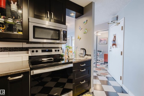 Kitchen featuring dark cabinetry, stainless steel appliances, light floors, and a textured ceiling - 1803 10149 Saskatchewan Drive, Edmonton, AB - Indoor Photo Showing Kitchen