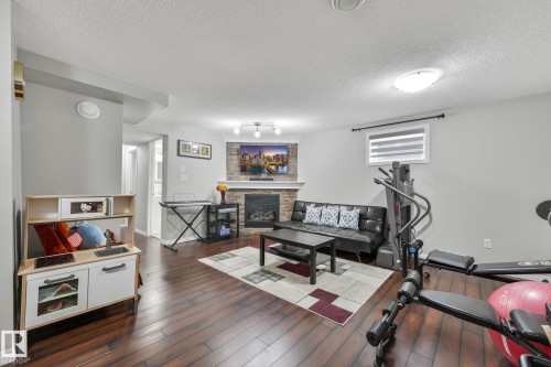 Workout area with a textured ceiling, dark wood-type flooring, and a stone fireplace - 2348 28B Avenue, Edmonton, AB - Indoor Photo Showing Other Room With Fireplace