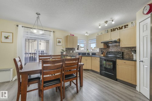 Kitchen featuring black range with electric stovetop, dark countertops, light wood finish cabinetry, tasteful backsplash, and light wood-style flooring - 2348 28B Avenue, Edmonton, AB - Indoor