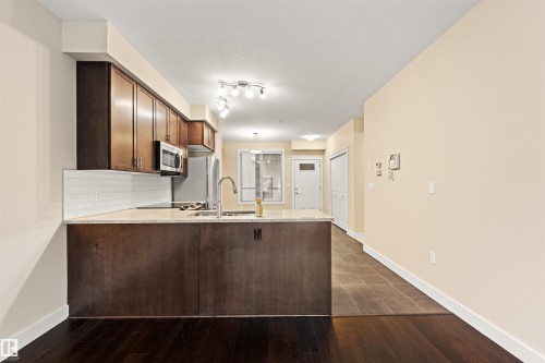 Kitchen with dark wood finish cabinetry, a peninsula, dark wood-style floors, stainless steel appliances, and light stone countertops - 29 11518 76 Avenue, Edmonton, AB - Indoor Photo Showing Kitchen