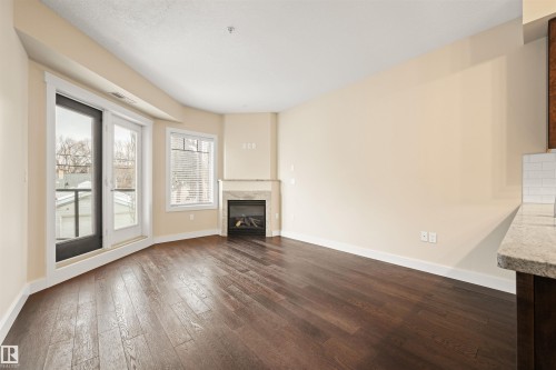 Unfurnished living room featuring dark wood-style floors and a premium fireplace - 29 11518 76 Avenue, Edmonton, AB - Indoor Photo Showing Other Room With Fireplace