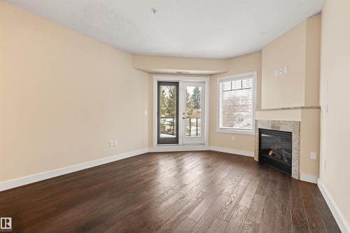 Unfurnished living room with a tiled fireplace and dark wood-style flooring - 29 11518 76 Avenue, Edmonton, AB - Indoor With Fireplace
