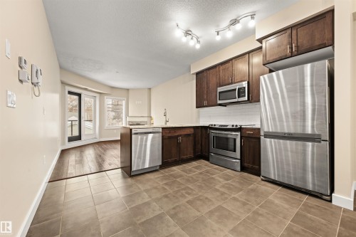 Kitchen featuring stainless steel appliances, dark wood finish cabinets, a peninsula, tasteful backsplash, and light tile patterned floors - 29 11518 76 Avenue, Edmonton, AB - Indoor Photo Showing Kitchen With Stainless Steel Kitchen
