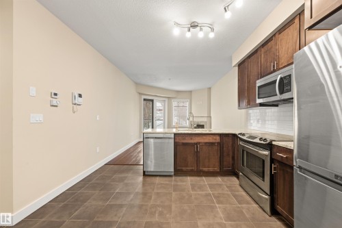 Kitchen with stainless steel appliances, a peninsula, light stone countertops, dark tile patterned flooring, and dark wood finish cabinetry - 29 11518 76 Avenue, Edmonton, AB - Indoor Photo Showing Kitchen With Upgraded Kitchen