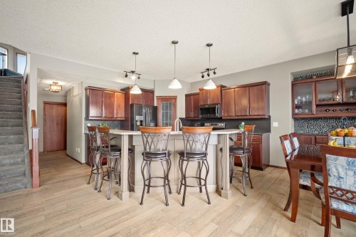 Kitchen featuring decorative backsplash, stainless steel appliances, a breakfast bar area, a center island with sink, and a textured ceiling - 19 Rosemount Boulevard, Beaumont, AB - Indoor