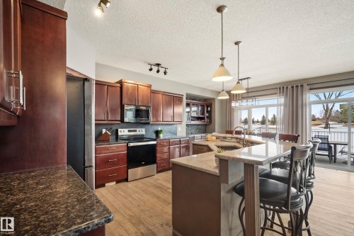 Kitchen featuring stainless steel appliances, track lighting, light wood-style flooring, dark stone counters, and a large island with sink - 19 Rosemount Boulevard, Beaumont, AB - Indoor Photo Showing Kitchen With Upgraded Kitchen